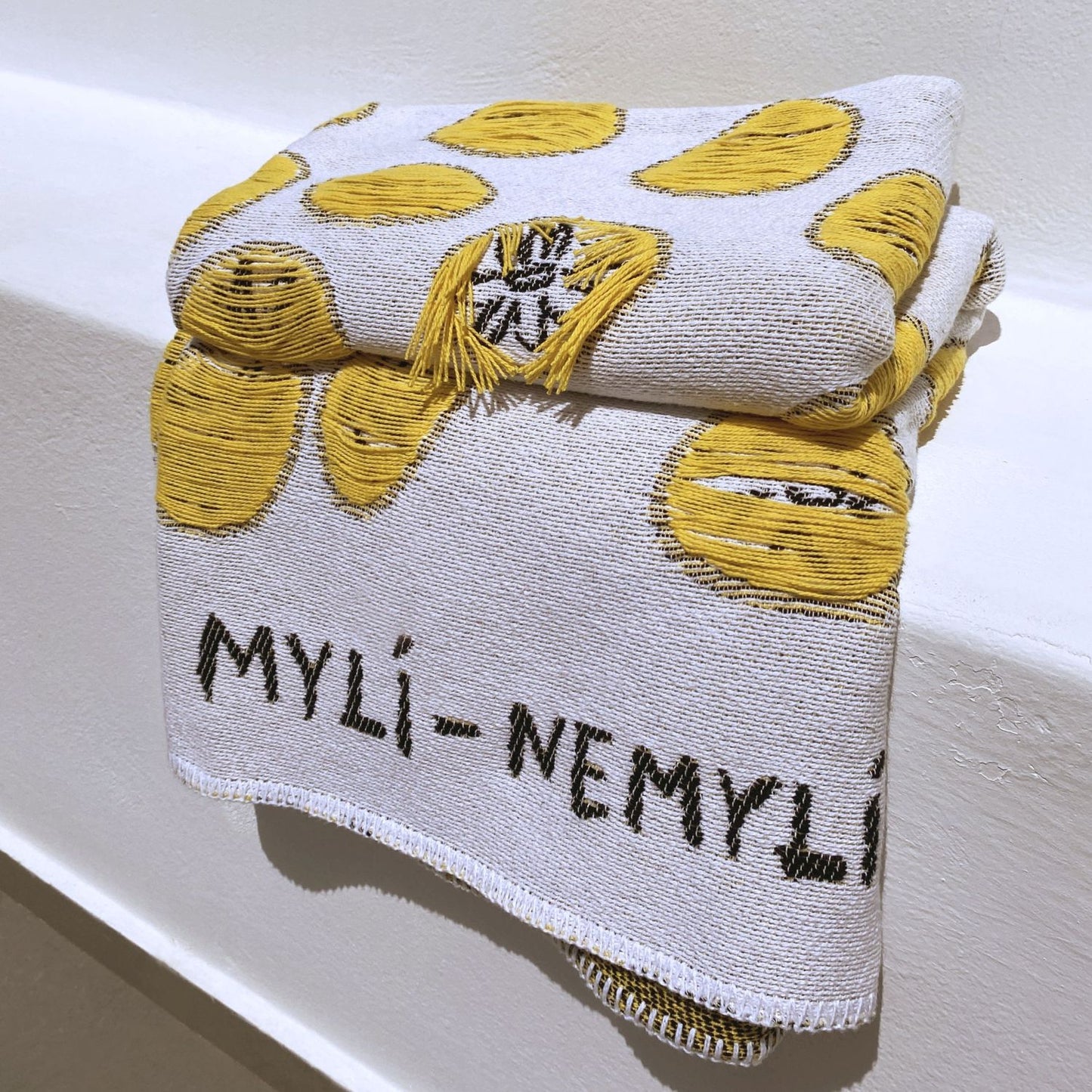 Textile with yellow patterns and 'MYLI-NEMYLI' text on a white background