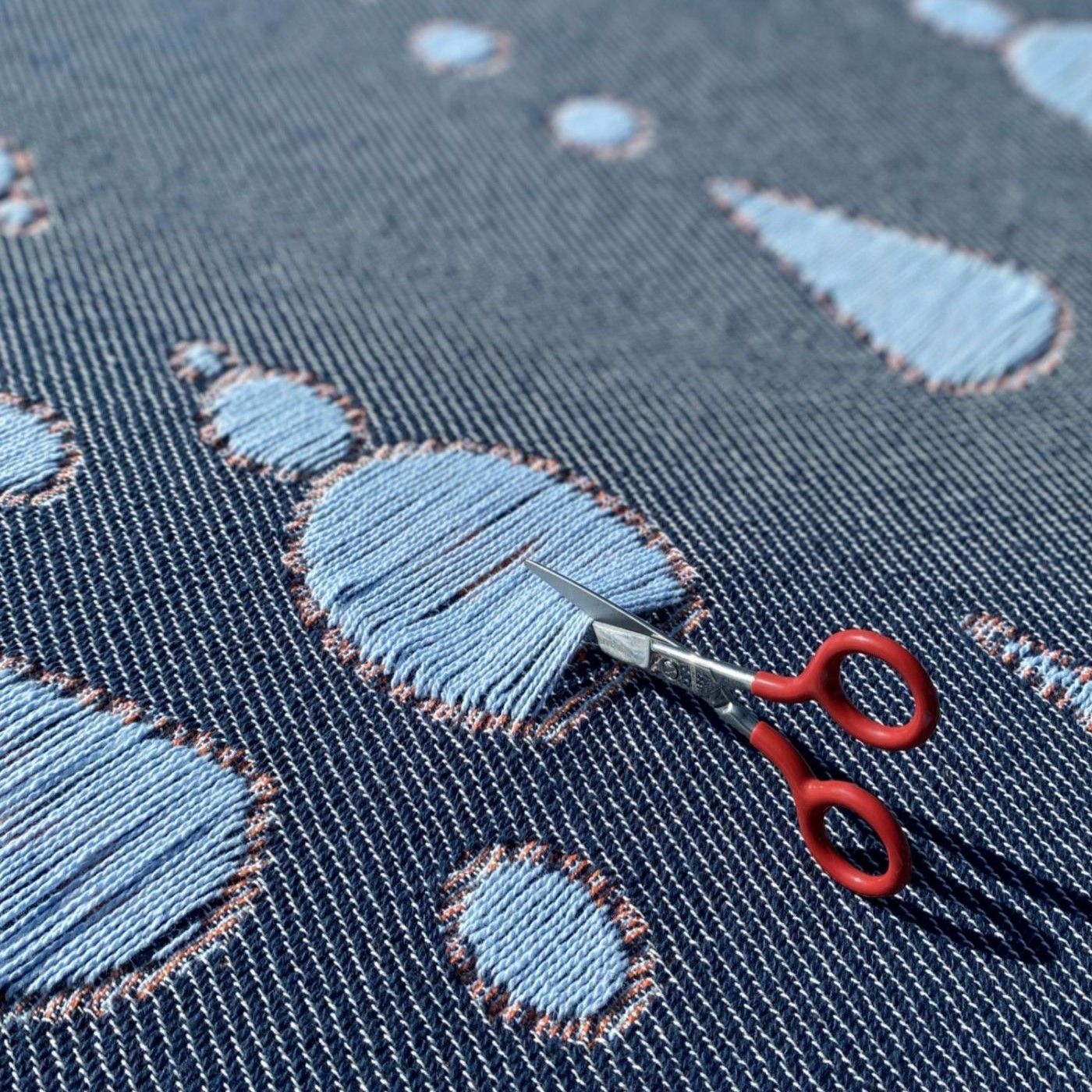 Scissors cutting the yarns of a interactive cotton blanket with a woven garden pattern, designed by Liucija Kostiva