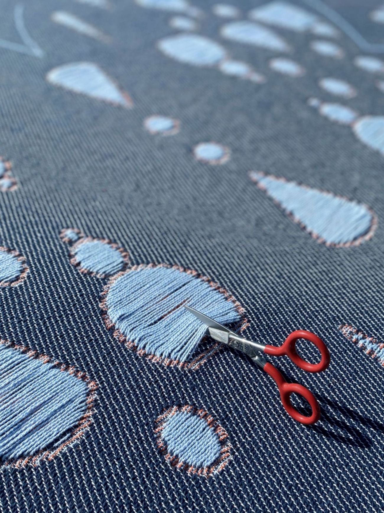 Scissors cutting the yarns of a cotton blanket with a woven garden pattern, designed by Liucija Kostiva