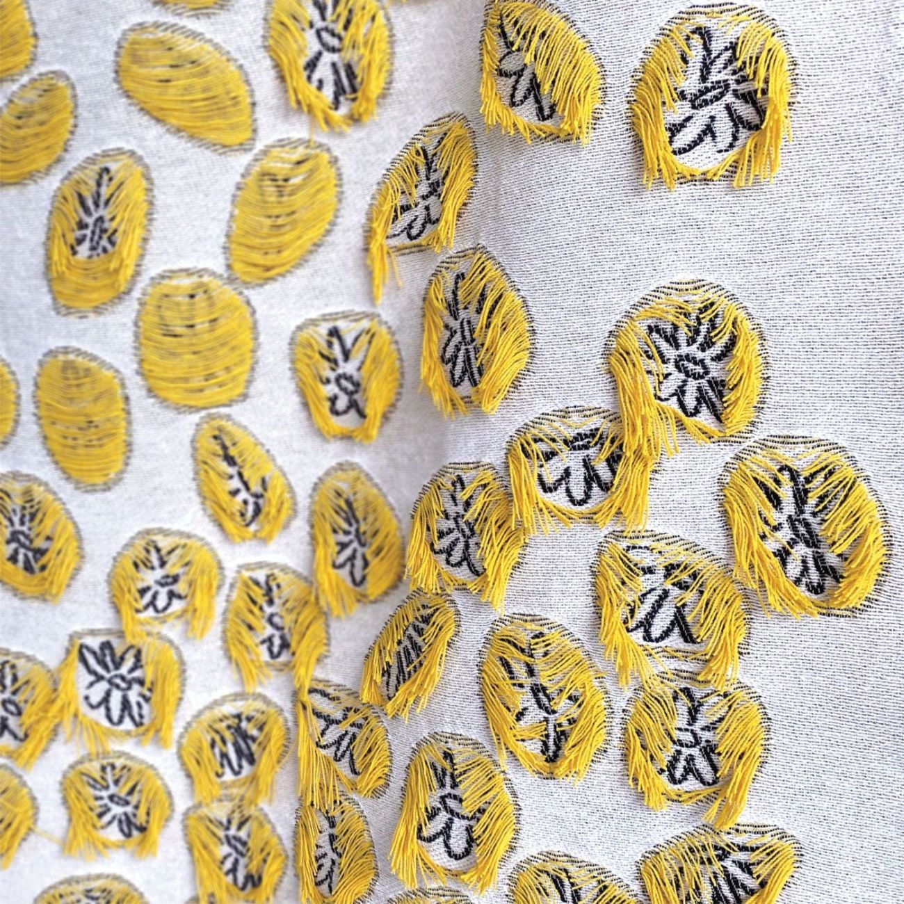 White cotton blanket with yellow patter of daisies, circular shapes and yarn fringes, designed by Liucija Kostiva