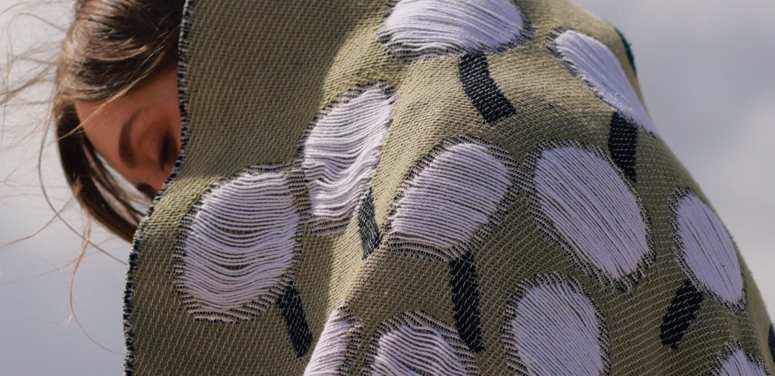 Mood image of person wearing olive green cotton blanket with abstract dandelion pattern designed by Liucija Kostiva