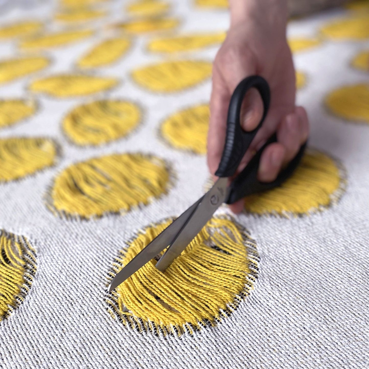 Scissors cutting the yarns of a cotton blanket with a woven circular pattern, designed by Liucija Kostiva