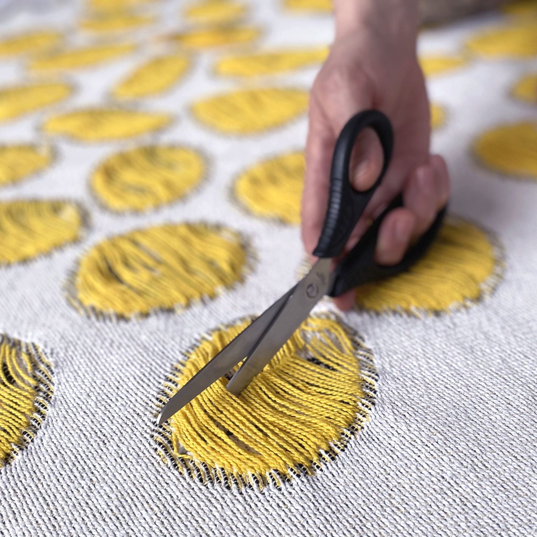 Scissors cutting the yarns of a cotton blanket with a woven circular pattern, designed by Liucija Kostiva