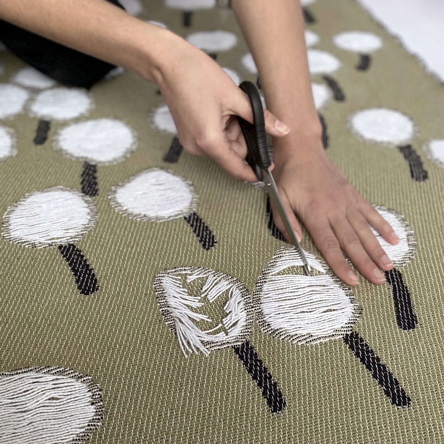 Scissors cutting the yarns of a cotton blanket with a woven dandelion pattern, designed by Liucija Kostiva