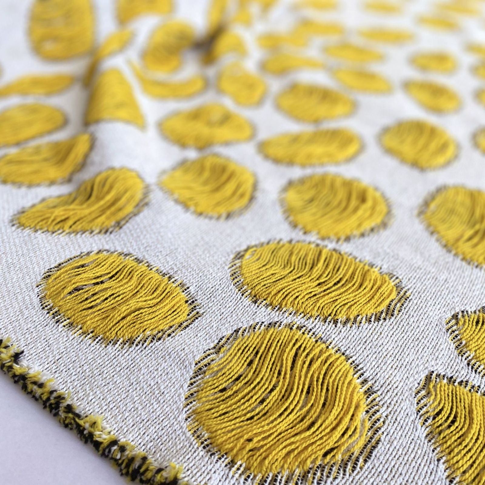 Closeup of cotton blanket with yellow circular patterns on a white background designed by Liucija Kostiva
